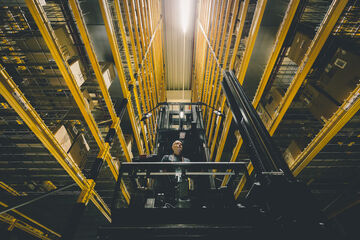A man on a narrow aisle forklift between two high racks