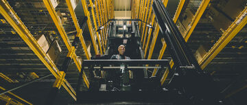 Ein Mann auf einem Schmalganggabelstapler zwischen zwei Hochregalen