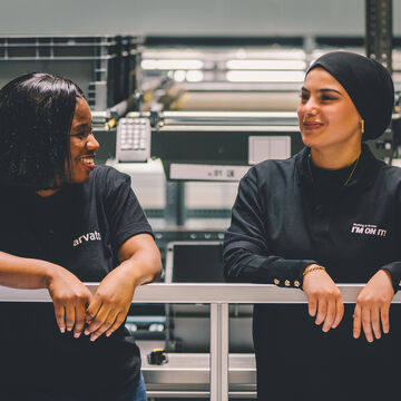 Two female employees lean casually against a railing and laugh with each other
