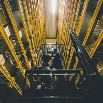 An employee on a narrow aisle stacker in the middle of two high racks